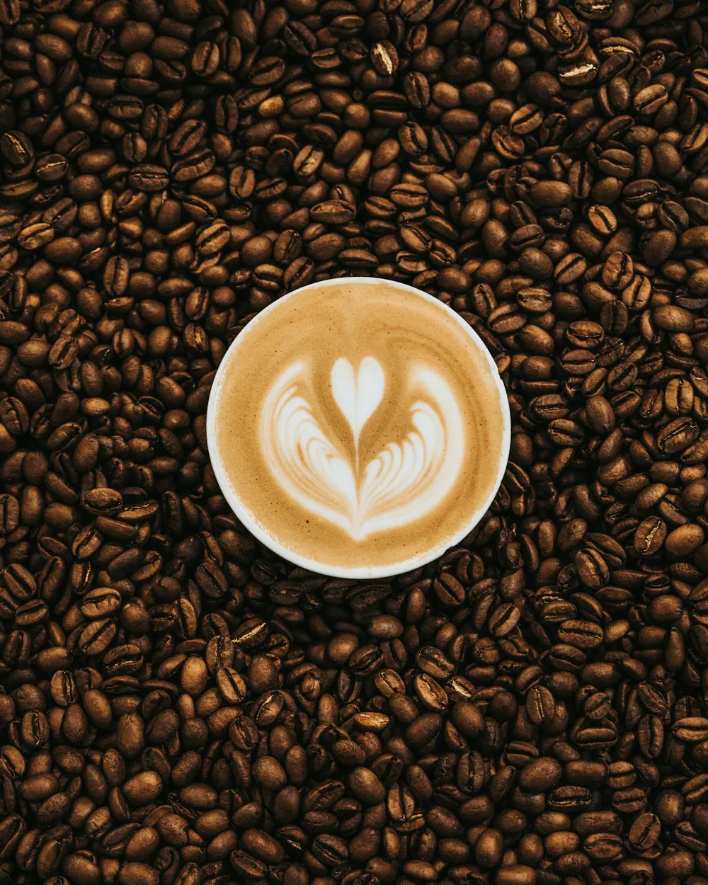 Latte art na šalici okruženoj zrnima kave